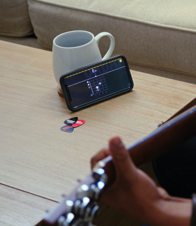 A person practicing guitar using the Urban App on their phone sitting on a coffee table.