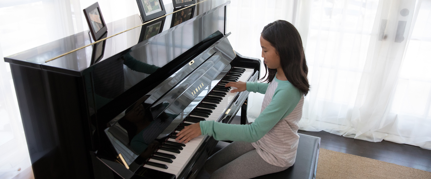 Young girl playing a Yamaha upright piano in her living room.