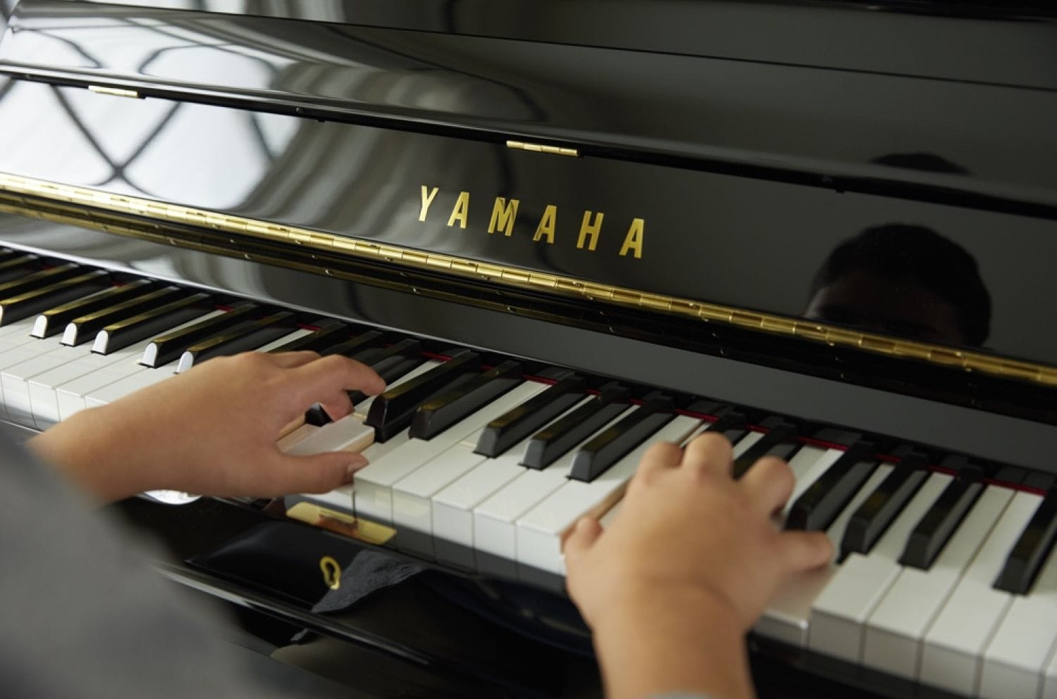 Child's hands playing a Yamaha upright piano.