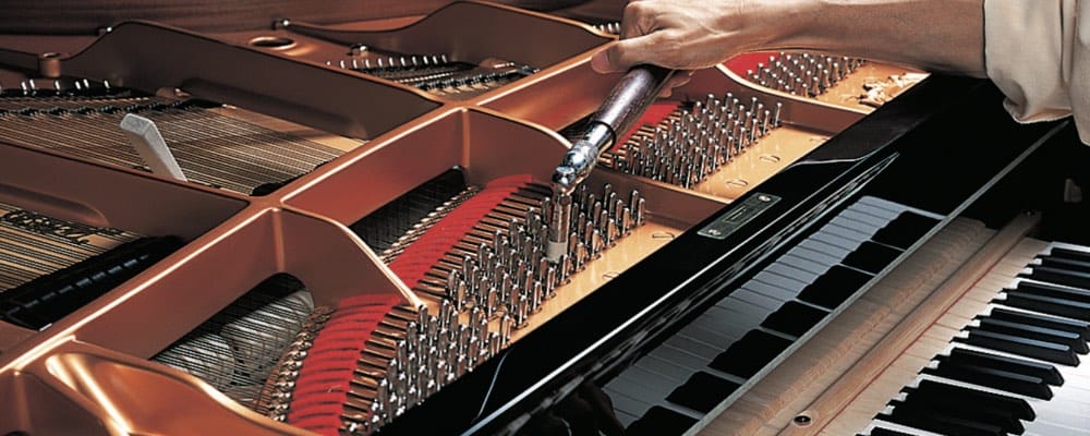 Someone is using a rachet tool to turn the pins that tighten or loosen the piano string in a …